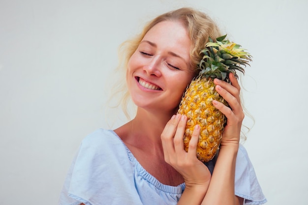 Porträt einer schönen blonden Frau mit blauen Augen, die Ananas auf weißem Hintergrund hält. Detox und Allergie gegen tropische Produkte