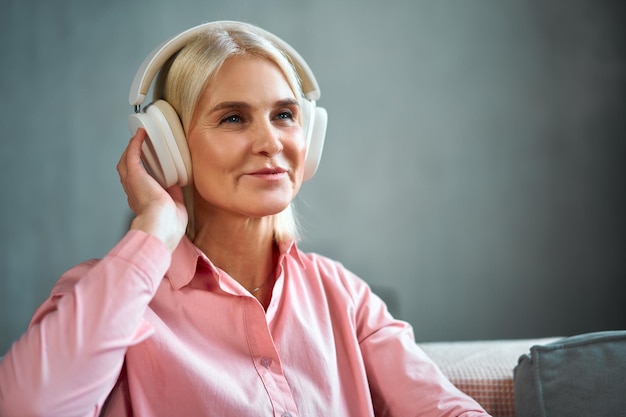 Foto porträt einer schönen blonden seniorin, die ihre kopfhörer zurechtrückt und lächelt. freizeitmusik und modernes leben im ruhestand