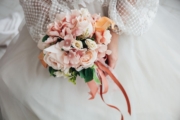 Porträt einer schönen Braut mit einem Blumenstrauß aus pastellorangefarbenen Hortensien und Rosen in ihren Händen in einem hellen Interieur