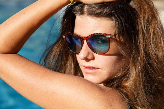 Porträt einer schönen Brünette mit Sonnenbrille und Pose im Pool