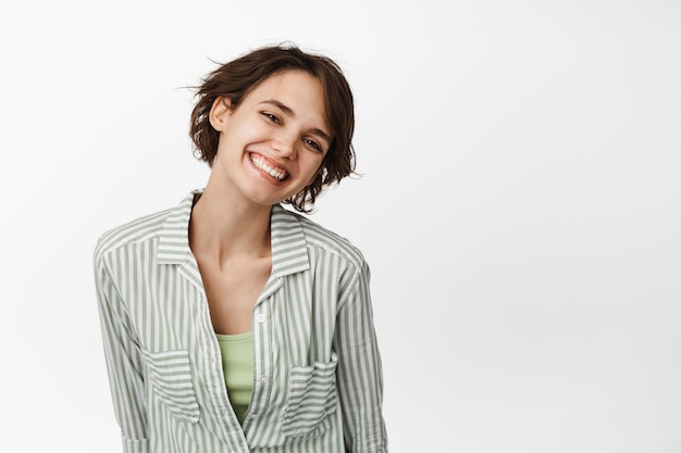 Porträt einer schönen brünetten Frau, eines Mädchens, das weiße Zähne lächelt und glücklich aussieht, zärtlich posiert und im Hemd auf weißem Hintergrund steht