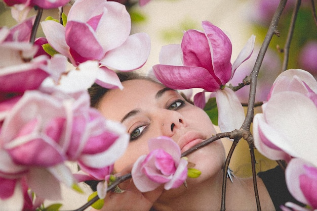 Porträt einer schönen Frau, die durch rosa Magnolienblumen gesehen wird