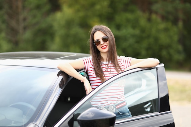 Porträt einer schönen Frau, die eine stilvolle schwarze Brille trägt und in der Nähe einer noblen Autobrünette posiert