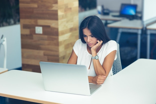 Porträt einer schönen Frau, die im Büro am Laptop arbeitet