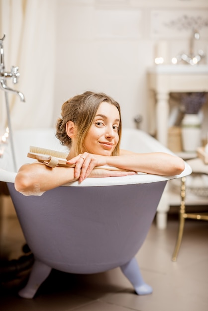 Porträt einer schönen Frau, die in der Retro-Badewanne des mit Kerzen verzierten Vintage-Badezimmers liegt