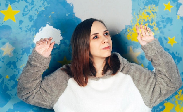 Porträt einer schönen Frau im Plüsch-Hoodie, die auf dem Hintergrund einer bunten, hellen Wand tanzt