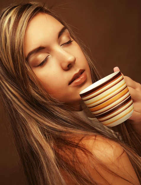 Porträt einer schönen Frau mit einer Tasse Kaffee, die auf dem beigen Hintergrund steht