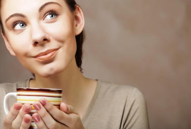 Porträt einer schönen Frau mit einer Tasse Kaffee, die auf dem beigen Hintergrund steht