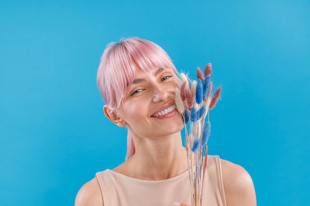 Porträt einer schönen Frau mit rosa Haaren, die in die Kamera lächelt und getrocknetes Pampasgras in der Hand hält