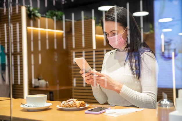 Porträt einer schönen Frau mittleren Alters, die mit einem Telefon in einem Café mit Blick durch das Glasfenster sitzt