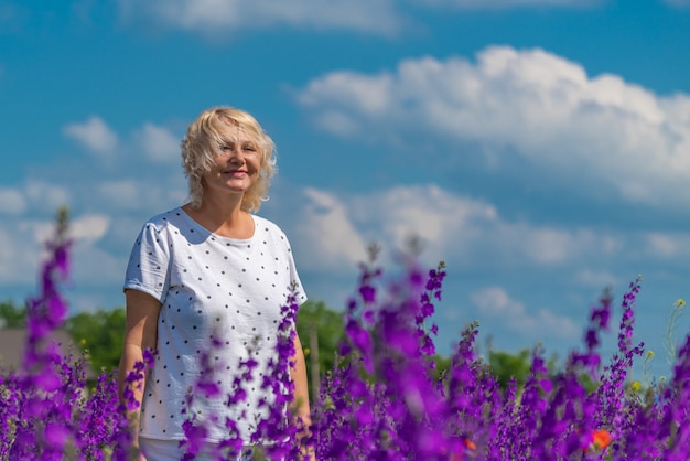 Porträt einer schönen glücklichen blonden Frau mittleren Alters in einem Feld mit blauem Himmel des Blumenhintergrundes