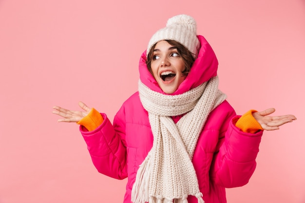 Porträt einer schönen glücklichen Frau in warmer Kleidung, die mit den Händen isoliert auf Rosa lächelt