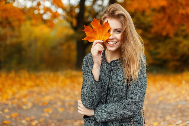 Porträt einer schönen glücklichen Frau mit einem Lächeln mit einem herbstgelben Blatt im Park