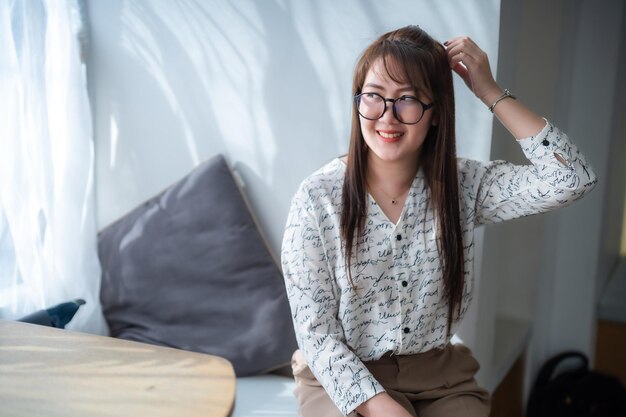 Porträt einer schönen, glücklichen, lächelnden, entspannten asiatischen Frau, die zu Hause im Wohnzimmer auf einer bequemen Couch sitzt