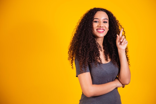 Porträt einer schönen jungen Afroamerikanerin mit lockigem Haar, die eine Idee auf gelbem Hintergrund mit Platz für Text denkt und hat. gute Idee Frau Konzept