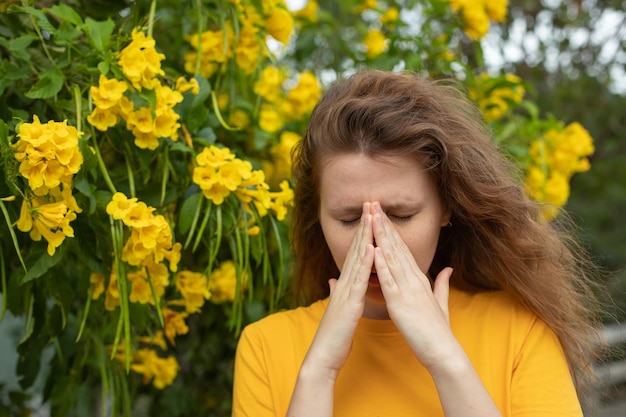 Porträt einer schönen jungen allergischen Frau leidet an Pollenallergie oder Erkältung auf natürlichem, blühendem Baumhintergrund im Frühling oder an sonnigen Sommertagen, die ihre laufende Nase bläst und die Augen reibt