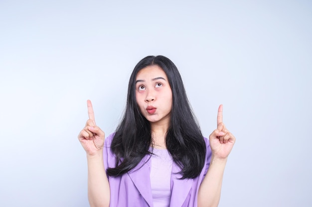 Porträt einer schönen jungen asiatischen Frau, die mit den Fingern auf den grauen Hintergrund zeigt