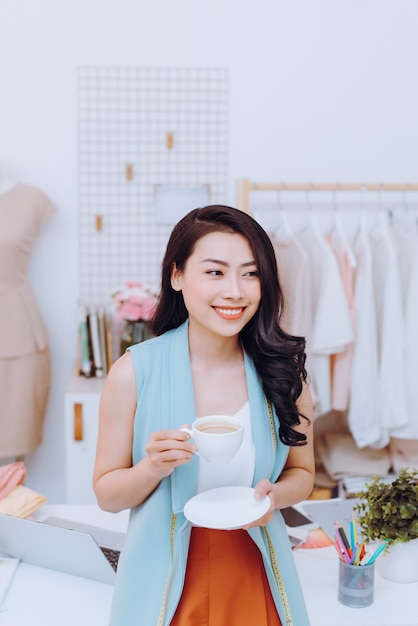 Porträt einer schönen jungen asiatischen Modedesignerin Geschäftsfrau in ihrem Studio beim Kaffeetrinken