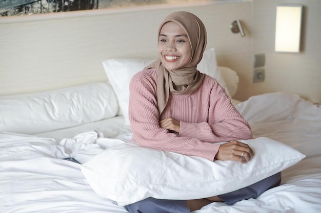 Porträt einer schönen jungen asiatischen muslimischen Frau mit Kopftuch auf einem Bett im Urlaub in einem Hotel