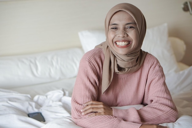 Porträt einer schönen jungen asiatischen muslimischen Frau mit Kopftuch auf einem Bett im Urlaub in einem Hotel