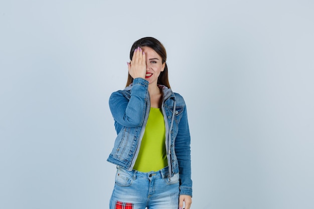 Porträt einer schönen jungen Dame, die im Denim-Outfit die Hand aufs Auge hält