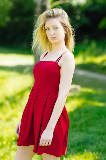 Foto porträt einer schönen jungen frau, die ein rotes kleid trägt, während sie im park steht