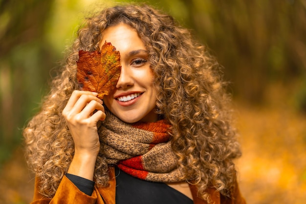 Porträt einer schönen jungen Frau, die sich im Freien unter gelben Blättern versteckt
