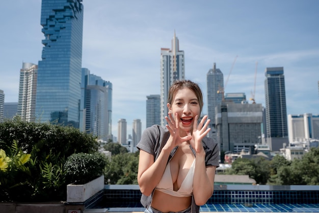 Porträt einer schönen jungen Frau, die sich mit Blick auf die Stadt entspannt und einen weißen Bikini und Jeans mit langen Beinen trägt