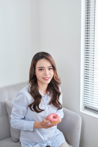 Porträt einer schönen jungen Frau, die zu Hause Donuts isst.