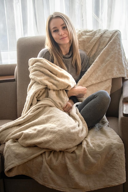 Porträt einer schönen jungen Frau, die zu Hause friert und sich in eine Decke hüllt, um sich warm zu halten