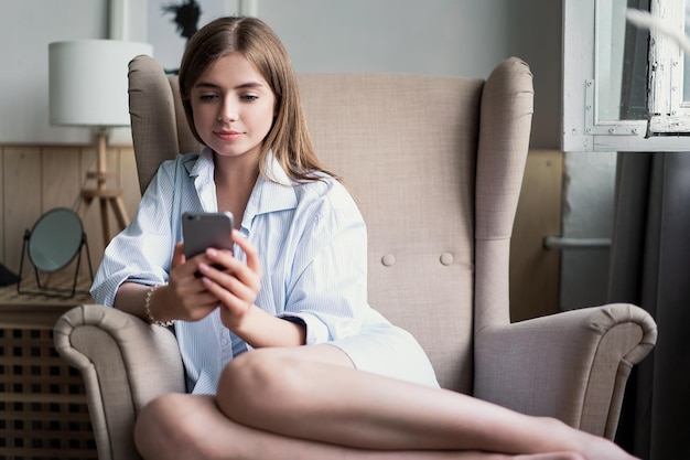 Porträt einer schönen jungen Frau, die zu Hause ihr Handy benutzt