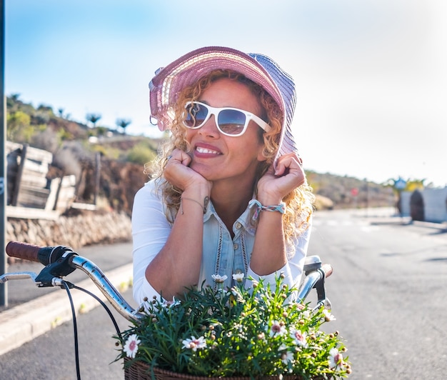 Porträt einer schönen jungen Frau, Hippie-Stil, Fahrrad im Freien unter dem Sonnenlicht genießen. Palmen und Kakteen um sie herum. Blauer Himmel