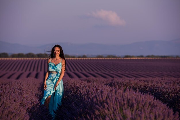 Porträt einer schönen jungen Frau in Cyand-Kleid, die sich entspannt und Spaß am Wind auf dem lila Lavendelblumenfeld hat