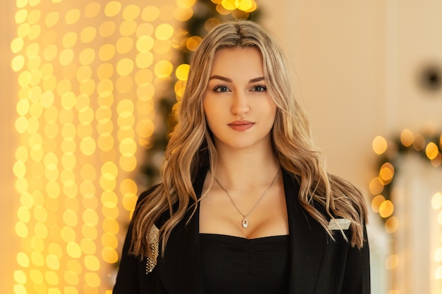 Porträt einer schönen jungen Frau in einem eleganten, modischen schwarzen Anzug mit einem Blazer auf einem Hintergrund gelber Bokeh-Lichter