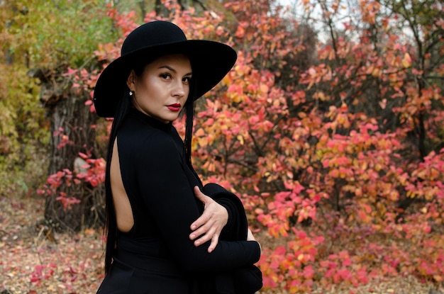 Porträt einer schönen jungen Frau in einem Herbstpark mit schwarzem Hut