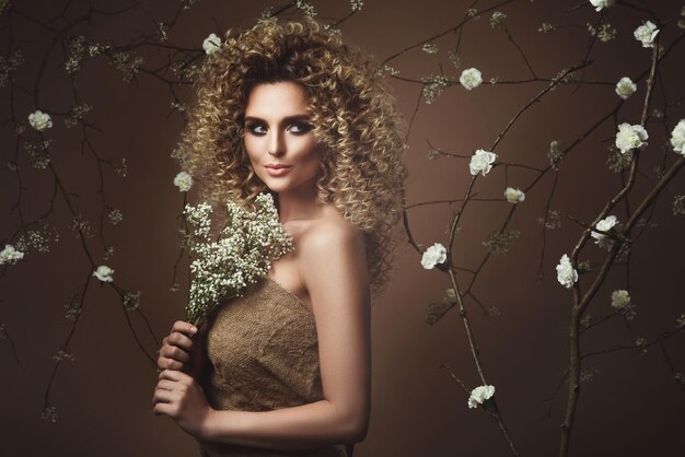 Porträt einer schönen jungen Frau mit Afro-Frisur und schönem Make-up mit vielen weißen Blumen im Hintergrund