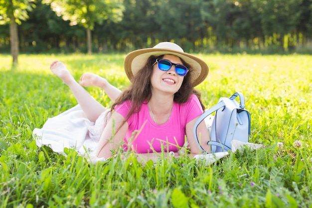 Porträt einer schönen jungen Frau mit Hut und Sonnenbrille, die beim Picknick im Park liegt?