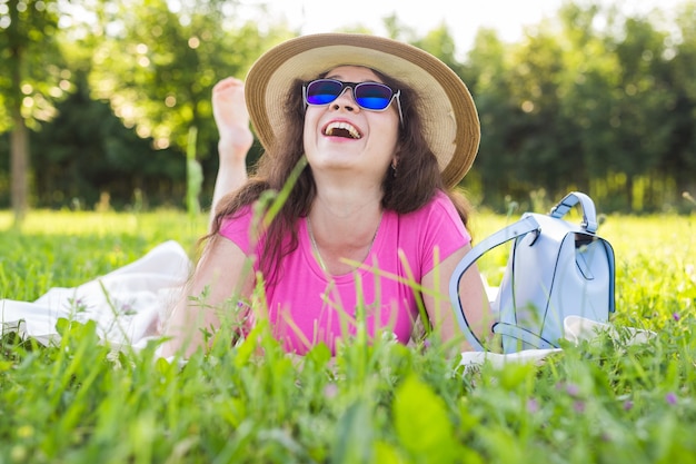 Porträt einer schönen jungen Frau mit Hut und Sonnenbrille, die beim Picknick im Park liegt?