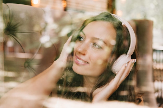 Porträt einer schönen jungen Frau mit Kopfhörern, die Musik hört, während sie in einem Straßencafé sitzt. Genießen Sie die Musikgeneration Z