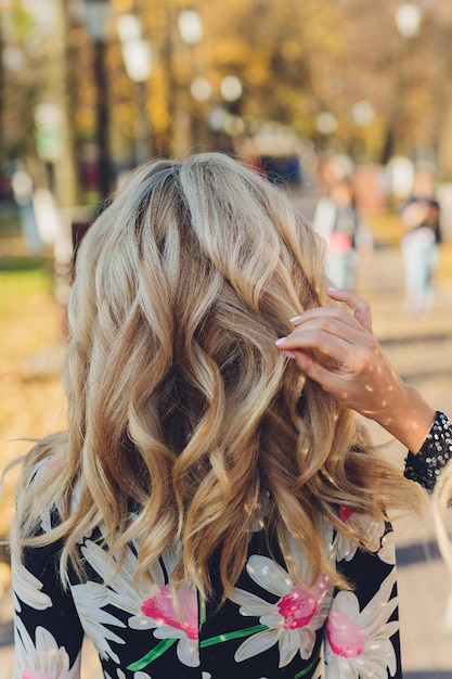 Porträt einer schönen jungen Frau mit langen blonden Haaren, die von hinten den Herbst im Park genießt. Hintergrund von Ginkgobäumen mit gelbem Laub. Herbstsaison