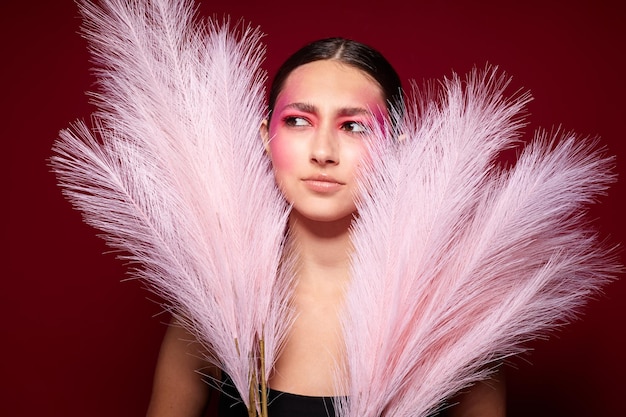 Porträt einer schönen jungen Frau mit rosafarbenen Federn, rosafarbenem Gesichtsmake-up, das einen attraktiven Blick auf rosa Hinterg