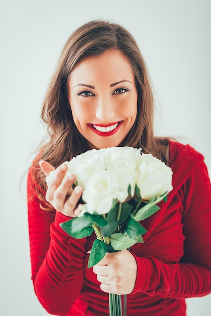 Porträt einer schönen jungen lächelnden Frau, die einen Strauß weißer Rosen hält und in die Kamera schaut.