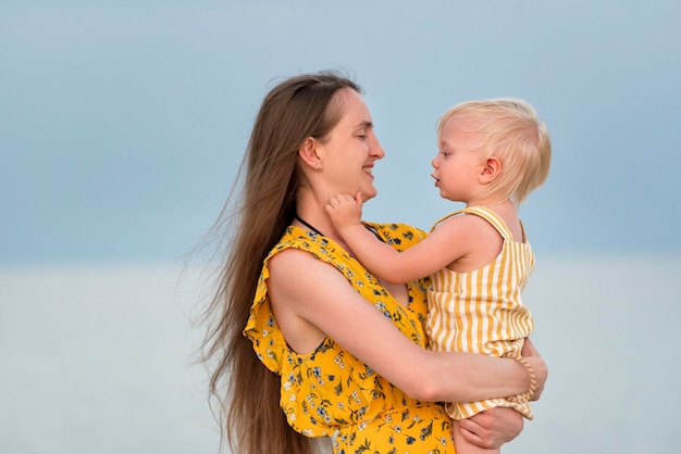 Porträt einer schönen jungen Mutter, die ihre kleine Tochter auf Meereshintergrund umarmt