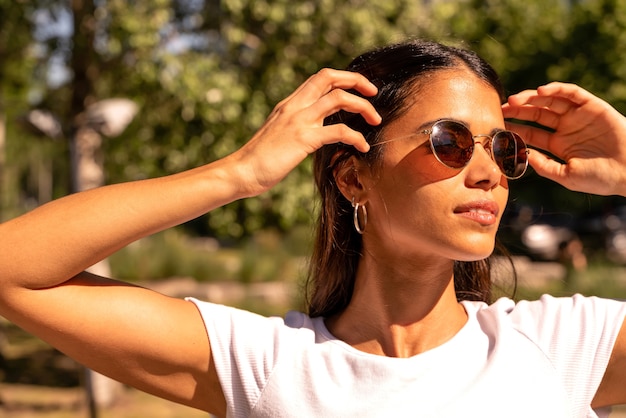 Porträt einer schönen lächelnden jungen Frau in einem weißen Hemd und in einer Sonnenbrille an einem sonnigen Tag