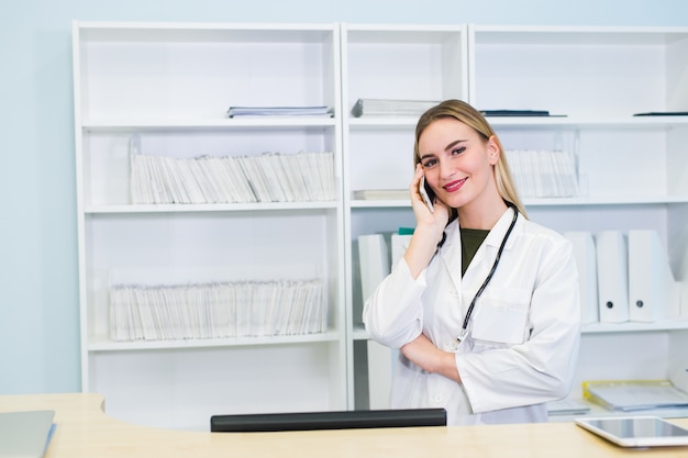 Porträt einer schönen lächelnden Krankenschwester an der Schreibtischstation beim Telefonieren und Ausfüllen eines medizinischen Informationsformulars