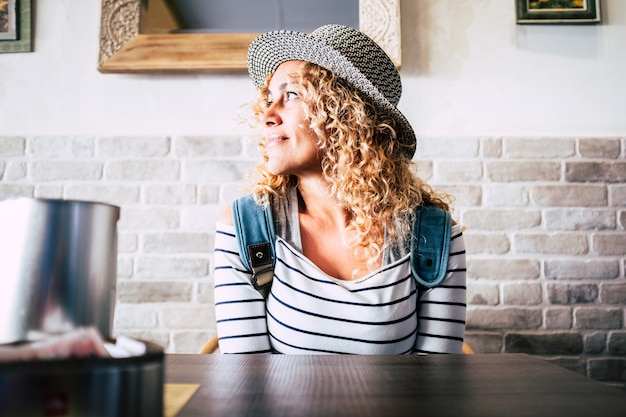 Porträt einer schönen lockigen Frau am Tisch des Restaurants, die denkt und träumt und lächelnd wegschaut