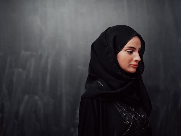 Porträt einer schönen muslimischen Frau in modischem Kleid mit Hijab vor einer schwarzen Tafel, die moderne islamische Mode und das Ramadan-Kareem-Konzept darstellt.