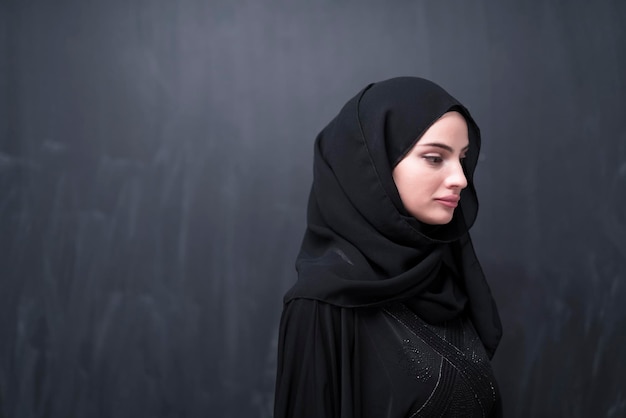 Porträt einer schönen muslimischen Frau in modischer Kleidung mit Hijab vor einer schwarzen Tafel, die moderne Islammode und Ramadan Kareem-Konzept darstellt.