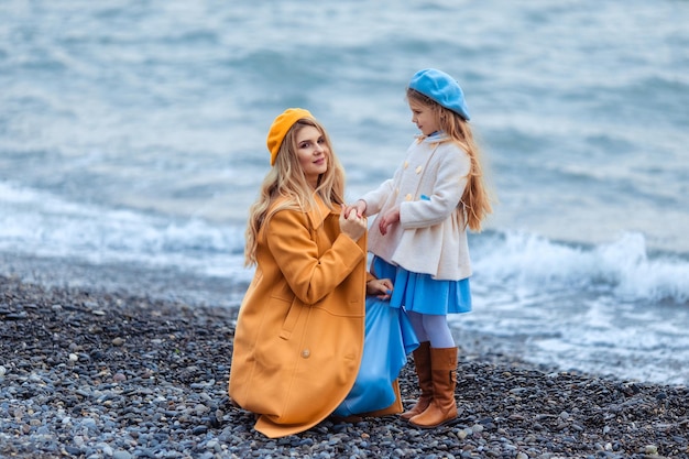 Porträt einer schönen Mutter und Tochter in warmer Kleidung an der Küste in der kalten Jahreszeit Familienspaziergang am Strand entlang