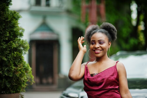 Porträt einer schönen natürlichen jungen afrikanischen Frau mit Afrohaar. Schwarzes Modell im roten Seidenkleid.